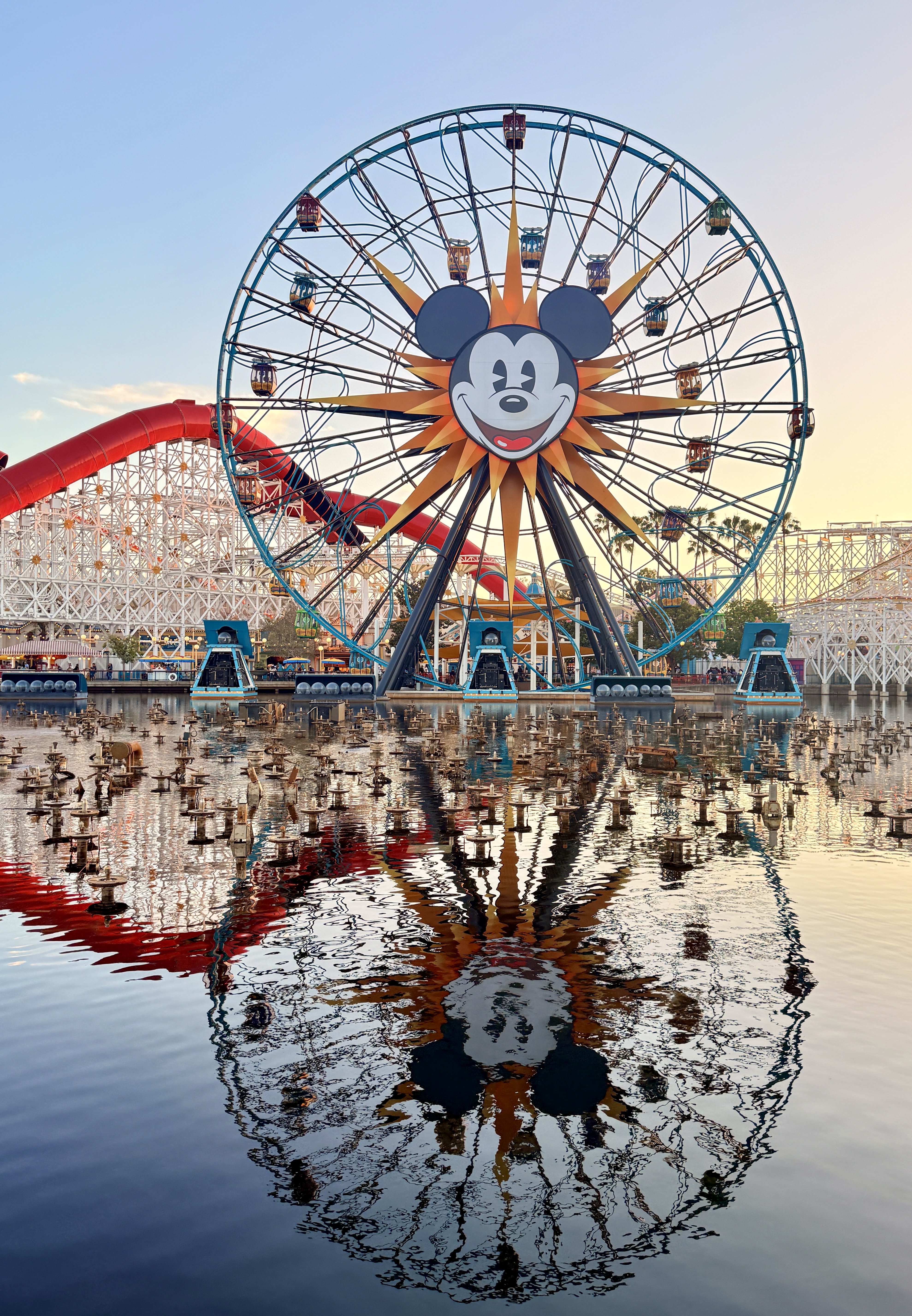Illuminated Pixar Pier wheel reflected in still water at dusk